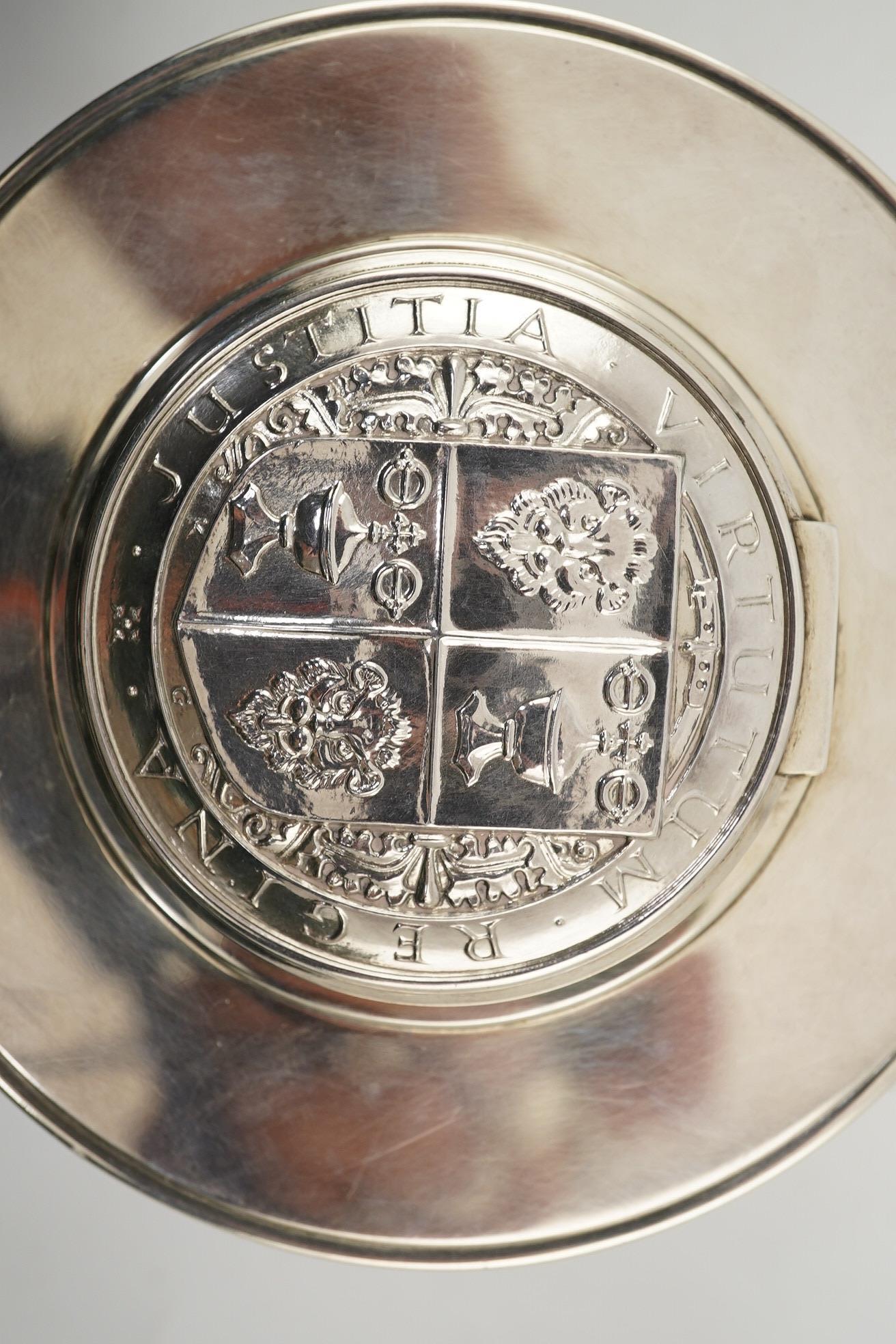 A George V silver circular inkwell, by Sebastian Garrard, commemorating the Silver Jubilee of King George V, the die stamped cover designed by George Kruger Gray featuring the Goldsmiths Company Coat of Arms